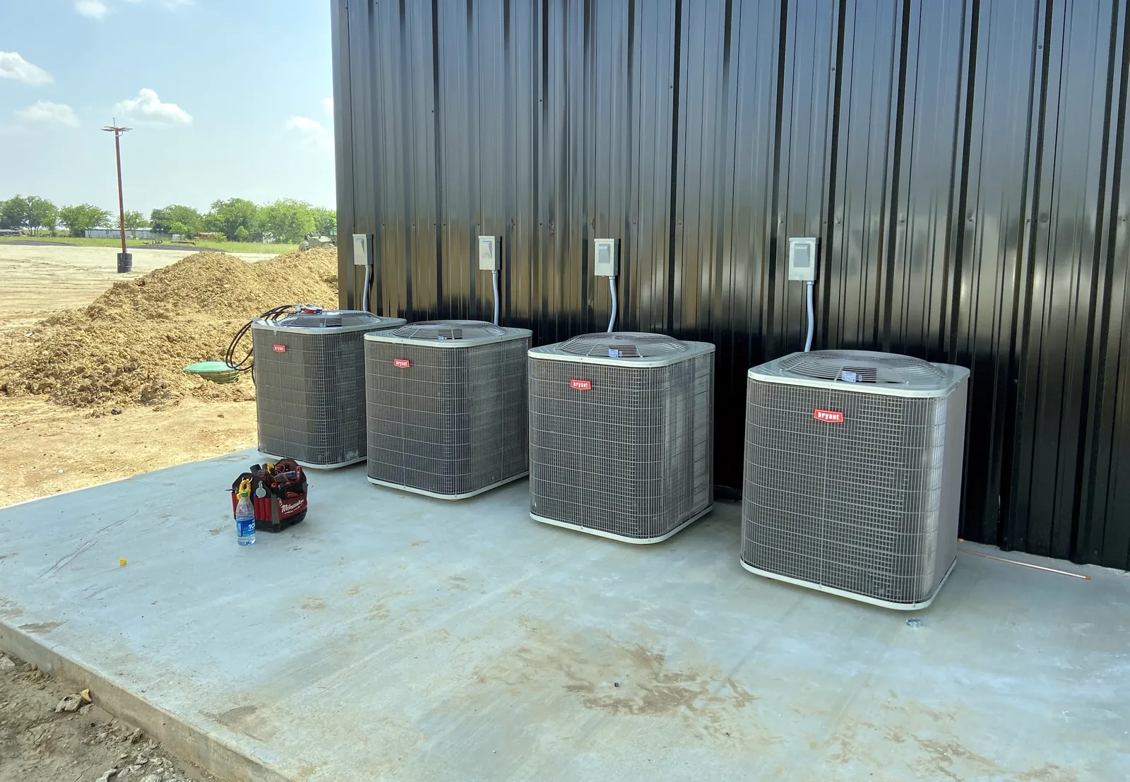 Four new Bryant condensers installed on a concrete pad beside a metal building