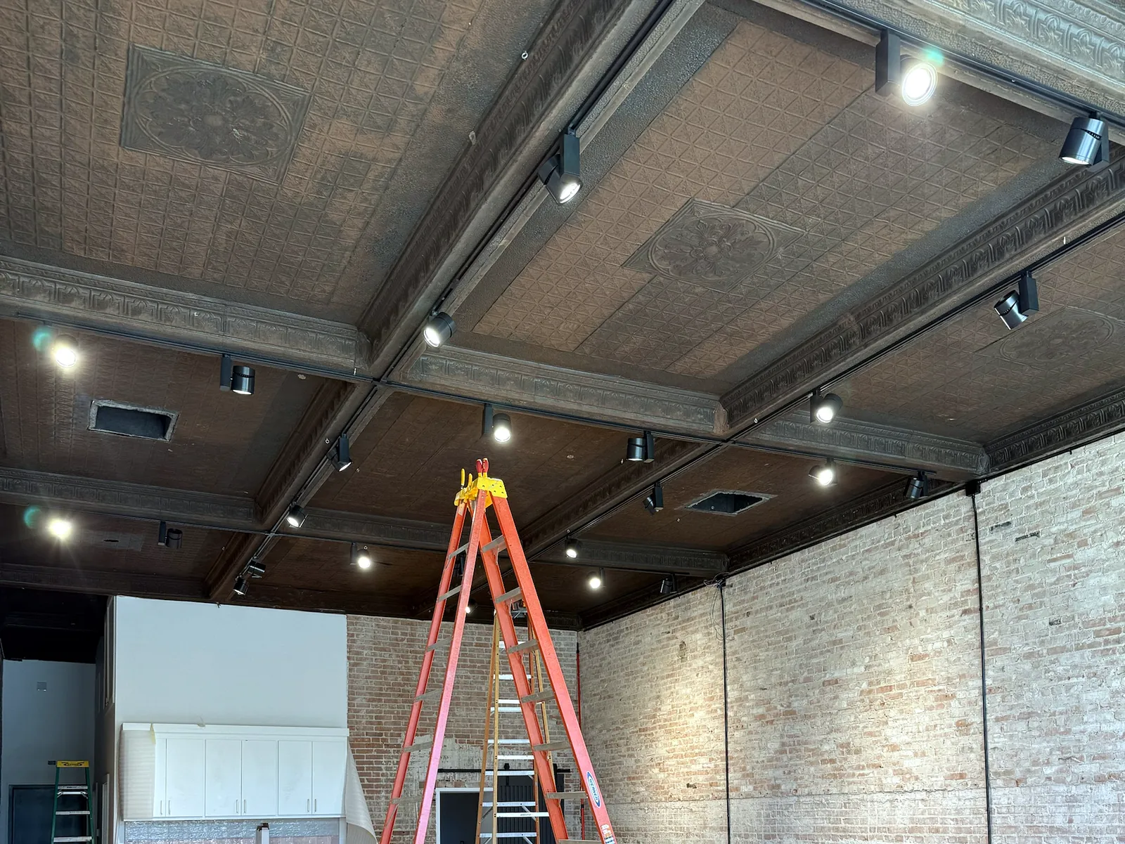 Track lighting installed under a pressed-tin ceiling in a commercial storefront